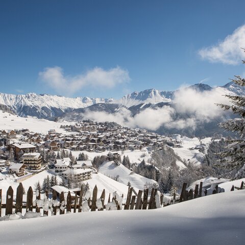Verschneite Aussicht auf die Ortschaft Serfaus mit Bergen im Hintergrund und einem Holzzaun im Vordergrund | © Serfaus-Fiss-Ladis Marketing GmbH | Andreas Kirschner