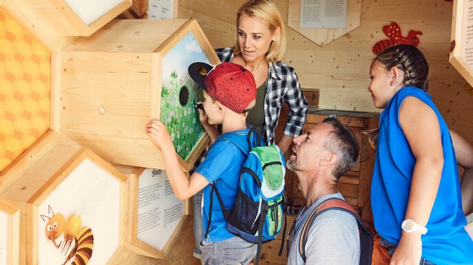 Familie mit zwei Kindern entdeckt interaktive Stationen rund um das Thema Bienen im Bienenhaus in Serfaus-Fiss-Ladis | © Seilbahn Komperdell | Christian Waldegger