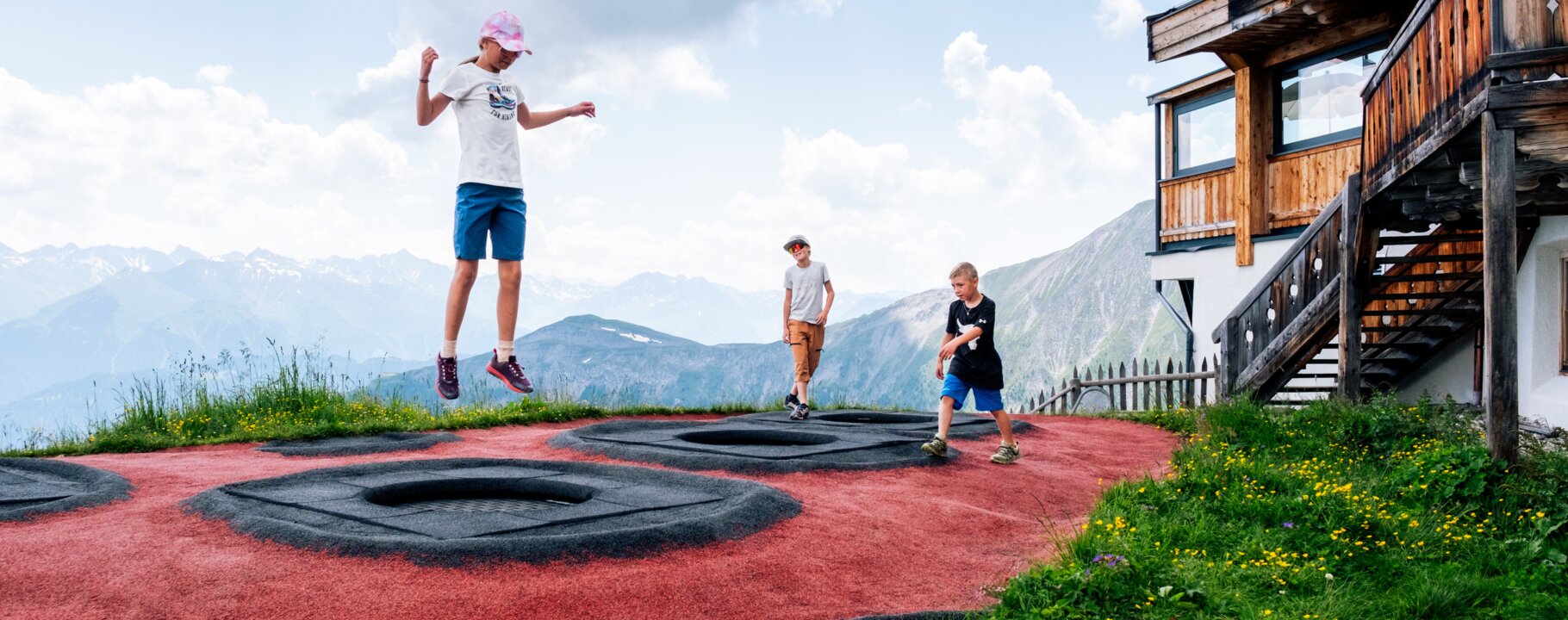 Kinder springen auf eingebauten Trampolinen bei der Kuhalm in Serfaus-Fiss-Ladis vor alpiner Bergkulisse | © Serfaus-Fiss-Ladis Marketing GmbH