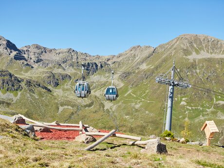 Zwei Gondeln schweben über einer alpinen Landschaft mit grünen Bergen in Serfaus-Fiss-Ladis | © Serfaus-Fiss-Ladis Marketing GmbH