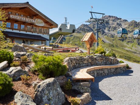 Sunny day at Lassida mountain restaurant with passing cable cars and view of the rocky Alps in Serfaus | © Christian Waldegger
