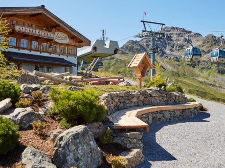 Sonniger Tag am Bergrestaurant Lassida mit vorbeifahrender Seilbahn und Blick auf die felsigen Alpen in Serfaus | © Christian Waldegger