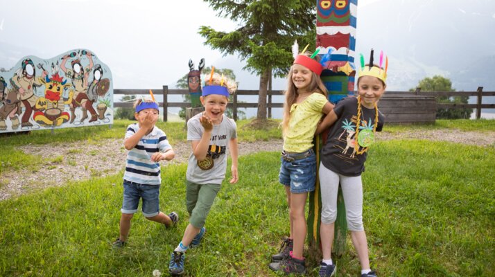 Fröhliche Kinder mit selbstgebastelten Indianer-Kopfschmuck spielen neben einem bemalten Totempfahl im Freien in Serfaus-Fiss-Ladis | © Andreas Kirschner