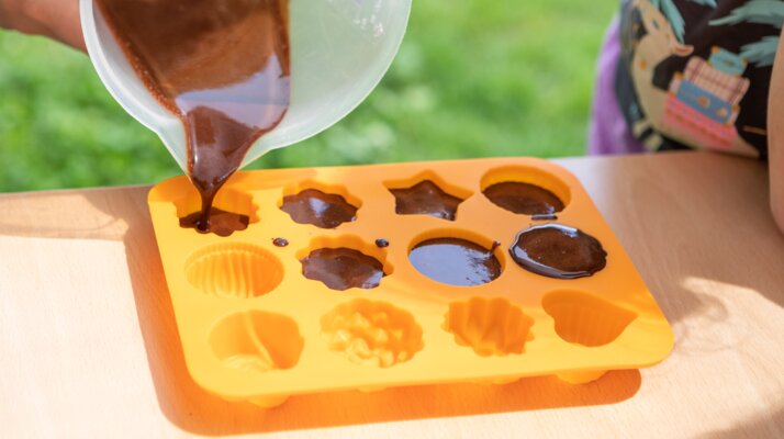 Chocolate mixture being poured by a child into colorful silicone molds, chocolate workshop in Serfaus-Fiss-Ladis | © Andreas Kirschner