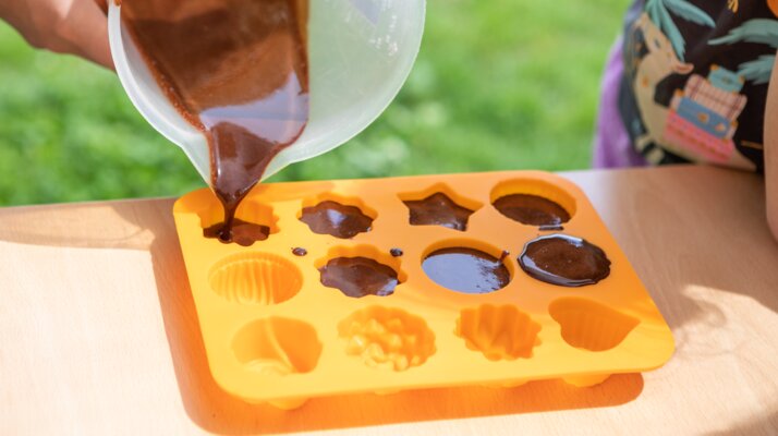 Schokoladenmasse wird von einem Kind in eine bunte Silikonform gegossen, Schokoladen-Workshop in Serfaus-Fiss-Ladis | © Andreas Kirschner