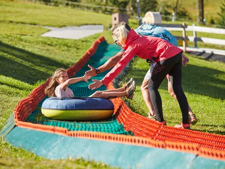 Mädchen rutscht mit einem Reifen die Sommerreifenbahn im Funpark Fiss hinunter, Eltern helfen beim Ausstieg | © Serfaus-Fiss-Ladis Marketing GmbH