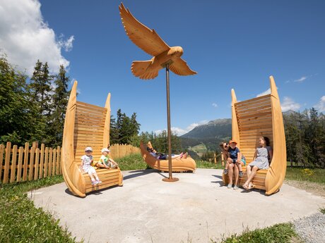 Familien entspannen auf Holzsitzen unter einer Adler-Skulptur inmitten der Natur | © Serfaus-Fiss-Ladis Marketing GmbH