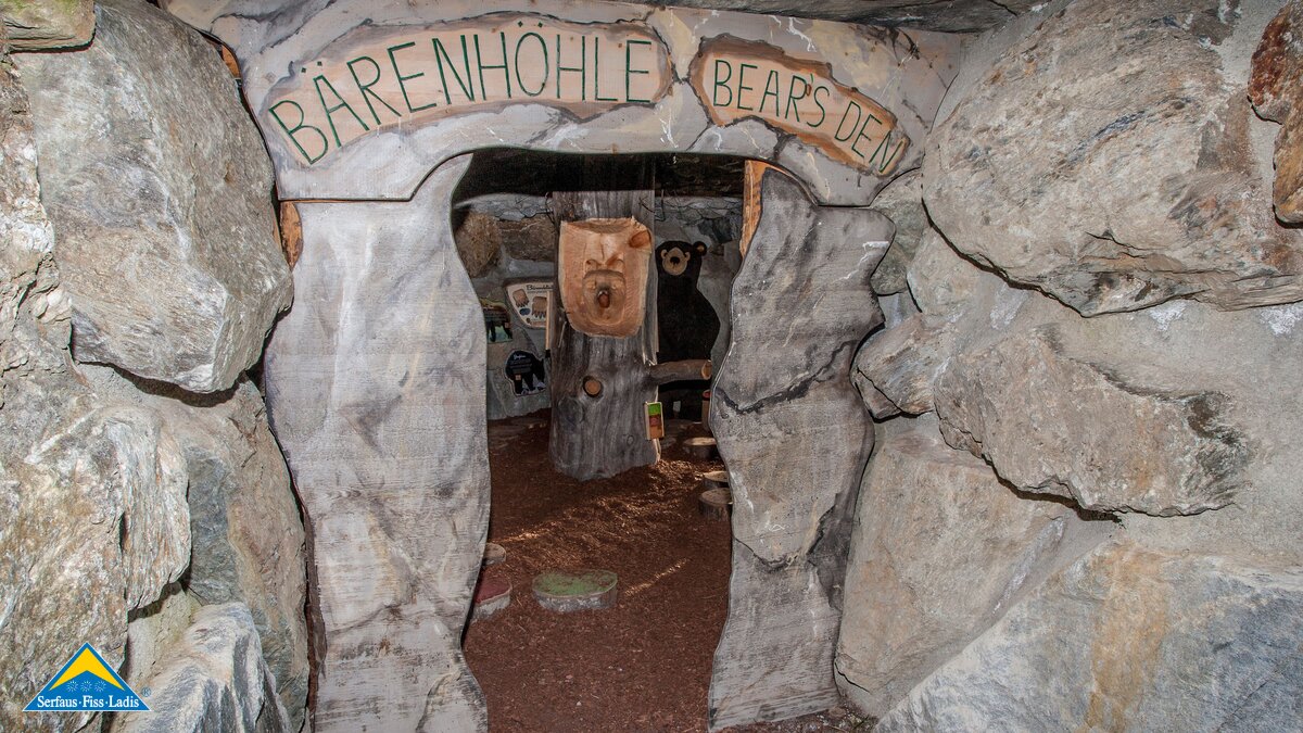 Höhleneingang mit Schriftzug „Bärenhöhle – Bears Den“ aus Felsnachbildung beim Wolfsee, im Inneren Bärendekoration und Baumstamm-Requisiten | © Serfaus-Fiss-Ladis Marketing GmbH