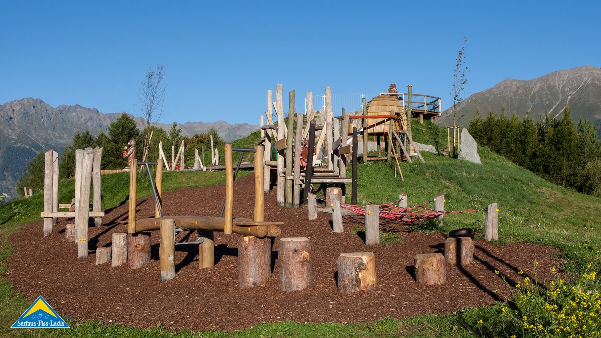 Spielplatz mit Holzstämmen, Balancierbalken und Rutsche inmitten einer grünen Berglandschaft in Serfaus-Fiss-Ladis | © Serfaus-Fiss-Ladis Marketing GmbH