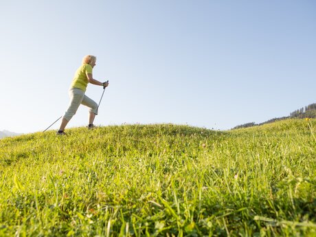 Frau beim Nordic Walking auf einer grünen Wiese an einem sonnigen Tag in Serfaus-Fiss-Ladis | © Serfaus-Fiss-Ladis Marketing GmbH | Andreas Kirschner