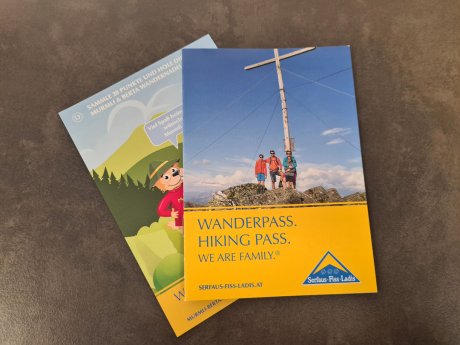 Zwei Flyer aus Serfaus-Fiss-Ladis – ein Wanderpass mit Gipfelkreuz-Motiv und ein Stempelheft mit Maskottchen Murmli | © Serfaus-Fiss-Ladis Marketing GmbH