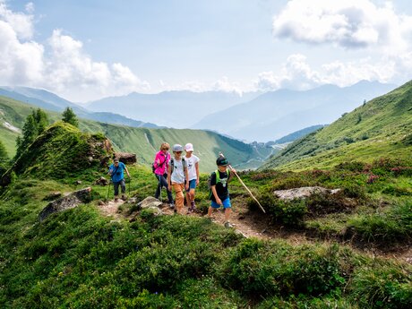 Eine Familie wandert auf einem schmalen Bergpfad durch grüne Almwiesen mit Aussicht auf das Alpenpanorama | © Serfaus-Fiss-Ladis Marketing GmbH | Manuel Kokseder