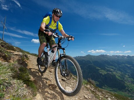Mann fährt mit dem Mountainbike auf einem schmalen Bergpfad in Serfaus-Fiss-Ladis mit weitem Blick ins Tal und umliegende Gipfel | © Serfaus-Fiss-Ladis Marketing GmbH