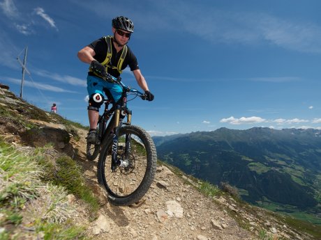Mountainbiker fährt auf einem schmalen alpinen Trail mit Panoramablick auf die Berge und Täler | © Serfaus-Fiss-Ladis Marketing GmbH