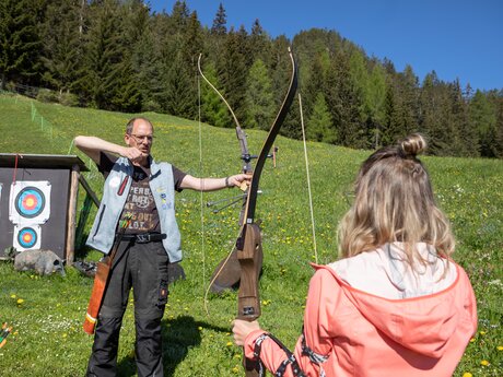 Bogenschießtrainer zeigt einer Teilnehmerin auf einer Almwiese in Serfaus-Fiss-Ladis die richtige Technik | © Serfaus-Fiss-Ladis Marketing GmbH | Andreas Kirschner