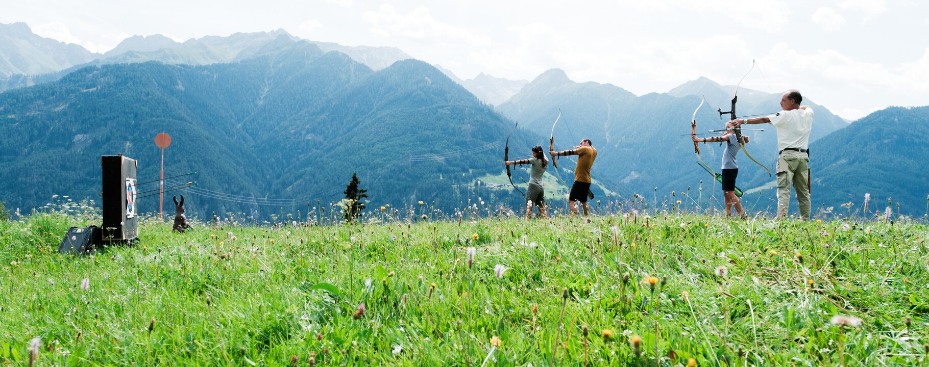 Vier Personen beim Bogenschießen auf einer grünen Almwiese in Serfaus-Fiss-Ladis mit Blick auf die Berge | © Serfaus-Fiss-Ladis Marketing GmbH | Andreas Kirschner