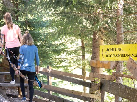 Zwei Frauen mit Bögen in der Hand gehen auf einem Waldweg zur Bogensportanlage in Serfaus-Fiss-Ladis | © Serfaus-Fiss-Ladis Marketing GmbH | Andreas Kirschner