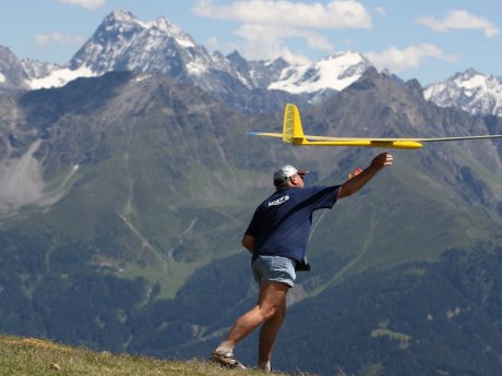Mann in Shorts und T-Shirt startet ein gelbes Modellflugzeug in Serfaus-Fiss-Ladis, im Hintergrund die schneebedeckten Alpen | © Serfaus-Fiss-Ladis Marketing GmbH