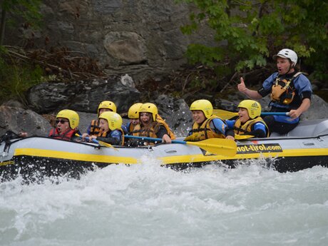 Gruppe von Kindern und einem Guide beim Rafting in Tirol, alle mit Helmen und Schwimmwesten auf einem Schlauchboot in wildem Wasser | © whynot-tirol.com
