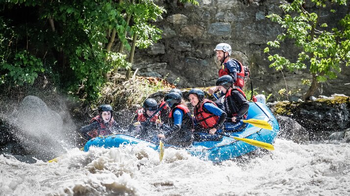 Gruppe mit Helmen und Schwimmwesten beim Rafting in einem aufspritzenden Wildwasserfluss | © whynot-tirol.com