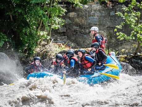 Gruppe mit Helmen und Schwimmwesten beim Rafting in einem aufspritzenden Wildwasserfluss | © whynot-tirol.com