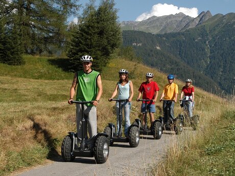 Fünf Personen fahren mit Helmen auf Segways einen schmalen Weg durch eine sommerliche Berglandschaft | © Serfaus-Fiss-Ladis Marketing GmbH