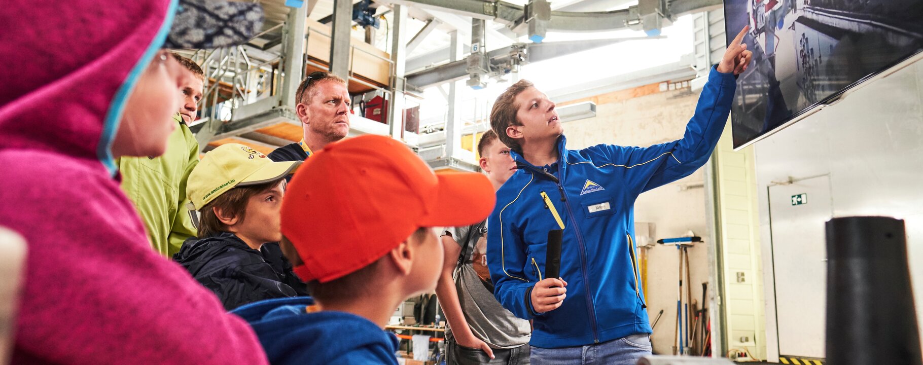 Gruppe von Kindern und Erwachsenen bei einer Technikführung, ein Mitarbeiter erklärt die Seilbahntechnik anhand eines Monitors | © Fisser Bergbahnen GmbH