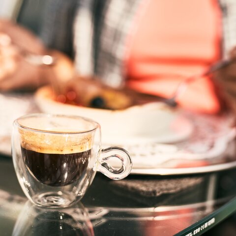 Close-up of an espresso cup on a glass table with a blurred background of a person dining at the Crystal Cube Serfaus-Fiss-Ladis | © Serfaus-Fiss-Ladis Marketing GmbH | Christian Waldegger