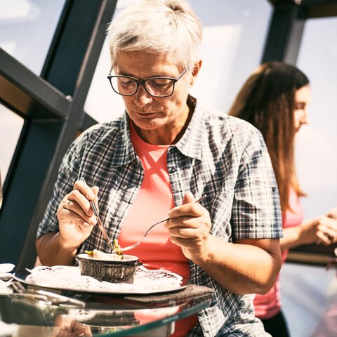 Elderly woman enjoying a meal at a glass table in the Crystal Cube in Serfaus-Fiss-Ladis, with a glass of wine beside her | © Serfaus-Fiss-Ladis Marketing GmbH | Christian Waldegger