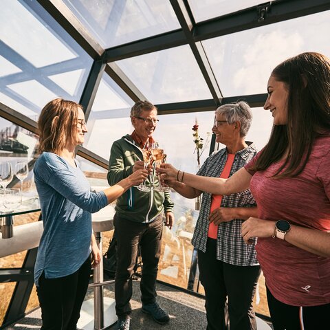 Four people clinking glasses in the glass-walled Crystal Cube in Serfaus-Fiss-Ladis, surrounded by panoramic mountain views | © Serfaus-Fiss-Ladis Marketing GmbH | Christian Waldegger