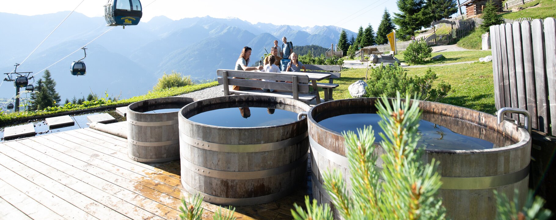 Holzbadewannen und Sitzplätze mit Aussicht auf Berge und vorbeifahrende Gondeln in Serfaus-Fiss-Ladis | © Serfaus-Fiss-Ladis Marketing GmbH | Andreas Kirschner