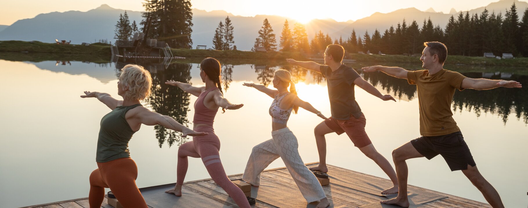 Gruppe beim Yoga am Seeufer in Serfaus-Fiss-Ladis bei Sonnenaufgang, umgeben von Bergen und Wäldern | © Serfaus-Fiss-Ladis Marketing GmbH | Daniel Zangerl