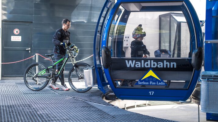 Ein Mountainbiker schiebt sein Fahrrad in eine blaue Waldbahn-Gondel in Serfaus-Fiss-Ladis | © Serfaus-Fiss-Ladis Marketing GmbH
