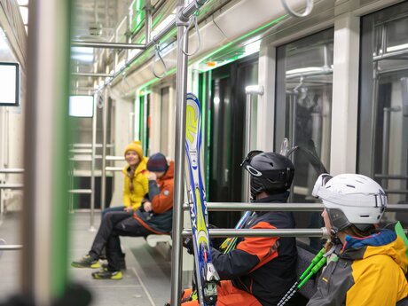Wintersportler in Skibekleidung mit Ski und Stöcken in der modernen U-Bahn von Serfaus, Tirol | © Serfaus-Fiss-Ladis Marketing GmbH | Andreas Kirschner
