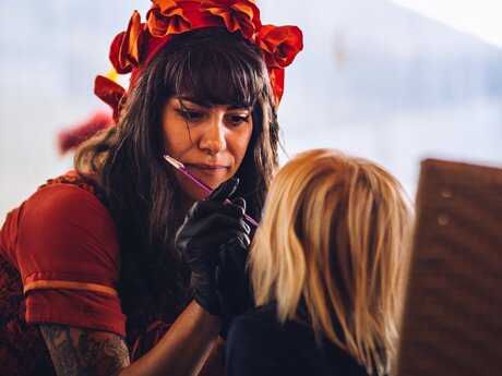 An artist in a red costume painting a small child's face at an event | © Serfaus-Fiss-Ladis Marketing GmbH