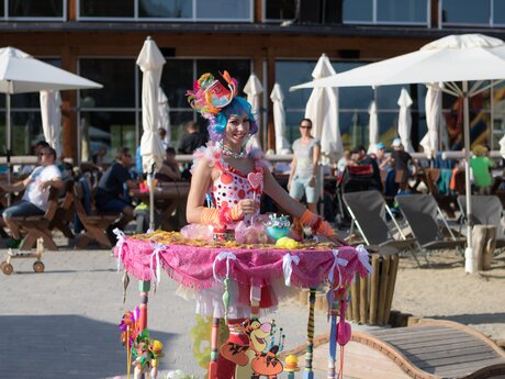 A colorfully dressed artist with a mobile candy stand at a beach event in the mountains | © Serfaus-Fiss-Ladis Marketing GmbH | Andreas Kirschner