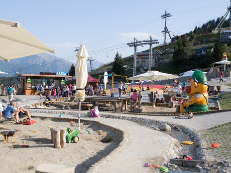 Children playing in a sand area with playground equipment and a bouncy castle near a mountain gondola station | © Serfaus-Fiss-Ladis Marketing GmbH