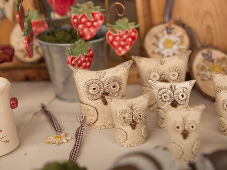 Mehrere kunstvoll gestaltete Keramik-Eulen stehen auf einem Tisch neben Dekorationen auf einem Kunsthandwerksmarkt | © Serfaus-Fiss-Ladis Marketing GmbH | Andreas Kirschner