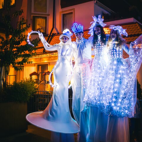 Stelzenläufer in leuchtenden Kostümen präsentieren eine Lichtershow bei Nacht vor beleuchtetem Gebäude | © Seilbahn Komperdell GmbH | Andreas Kirschner