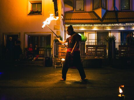 Ein Feuerkünstler führt bei Nacht auf einer Straße vor einem beleuchteten Gebäude eine Feuershow auf | © Serfaus-Fiss-Ladis Marketing GmbH | Andreas Kirschner