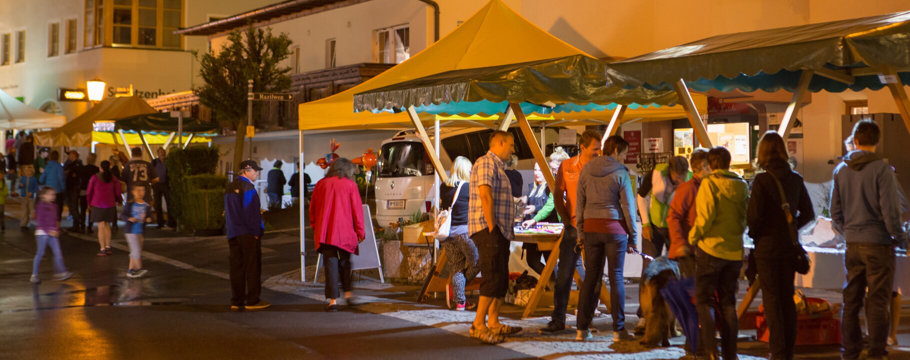 Menschen schlendern bei einem abendlichen Dorffest zwischen beleuchteten Marktständen im Ortszentrum | © Serfaus-Fiss-Ladis Marketing GmbH | Andreas Kirschner