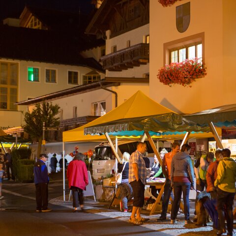 Menschen schlendern bei einem abendlichen Dorffest zwischen beleuchteten Marktständen im Ortszentrum | © Serfaus-Fiss-Ladis Marketing GmbH | Andreas Kirschner