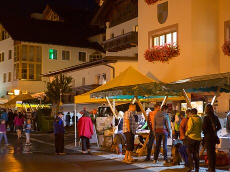 Menschen schlendern bei einem abendlichen Dorffest zwischen beleuchteten Marktständen im Ortszentrum | © Serfaus-Fiss-Ladis Marketing GmbH | Andreas Kirschner