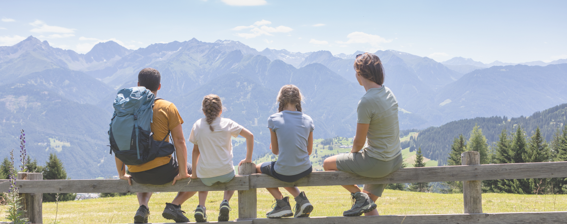 Zwei Kinder und ihre Eltern hocken auf einem Zaun und schauen sich eine Tallandschaft an | © Serfaus-Fiss-Ladis Marketing GmbH | Andreas Kirschner