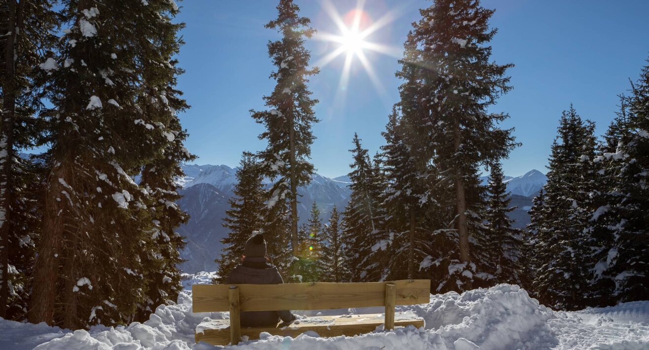 Eine Bank, am Wegesrand von Serfaus-Fiss-Ladis, mit einem schönen Ausblick auf die umliegenden Bäume und die Tiroler Bergwelt | © Serfaus-Fiss-Ladis Marketing GmbH I Andreas Kirschner
