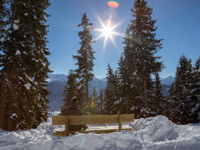 Eine Bank, am Wegesrand von Serfaus-Fiss-Ladis, mit einem schönen Ausblick auf die umliegenden Bäume und die Tiroler Bergwelt | © Serfaus-Fiss-Ladis Marketing GmbH I Andreas Kirschner