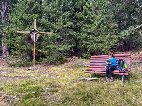 Holz-Bergkreuz mit Bank an einem Waldrand, umgeben von Bäumen und Wurzeln | © Serfaus-Fiss-Ladis Marketing GmbH