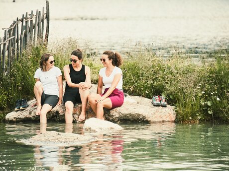 Urlauber sitzen auf einem Holzsteg am Ufer des Högsees in Serfaus, Schwimmen mit in den Bergen in der Region Serfaus-Fiss-Ladis Abkühlung in Tirol | © Serfaus-Fiss-Ladis Marketing GmbH | Christian Waldegger
