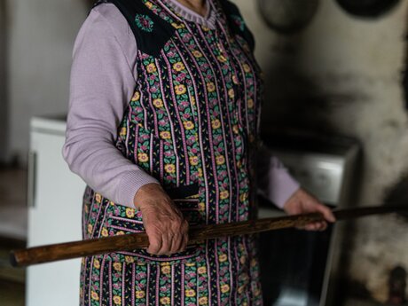 Frau mit langer Schaufel zum Einfeuern eines alten Holzofens Rosmarie Waldner im Gästemagazin Sun Days der Region Serfaus-Fiss-Ladis in Tirol | © Serfaus-Fiss-Ladis Marketing GmbH | Rene Raggl