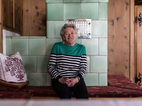 Maria Rietzler aus Fiss auf ihrer Ofenbank Beitrag Gästemagazin der Region Serfaus-Fiss-Ladis in Tirol Sun Days | © Serfaus-Fiss-Ladis Marketing GmbH | Rene Raggl